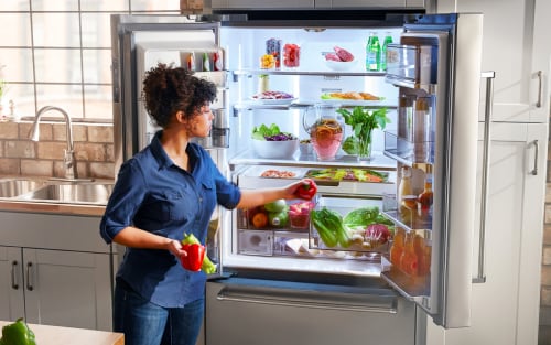 Woman loading vegetable into a french door refrigerator.