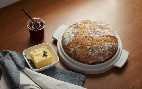 A round loaf of crusty bread with butter and honey on the side