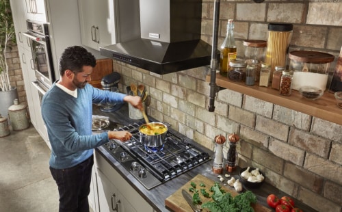 Man stirring a dish on a gas range with hood overhead