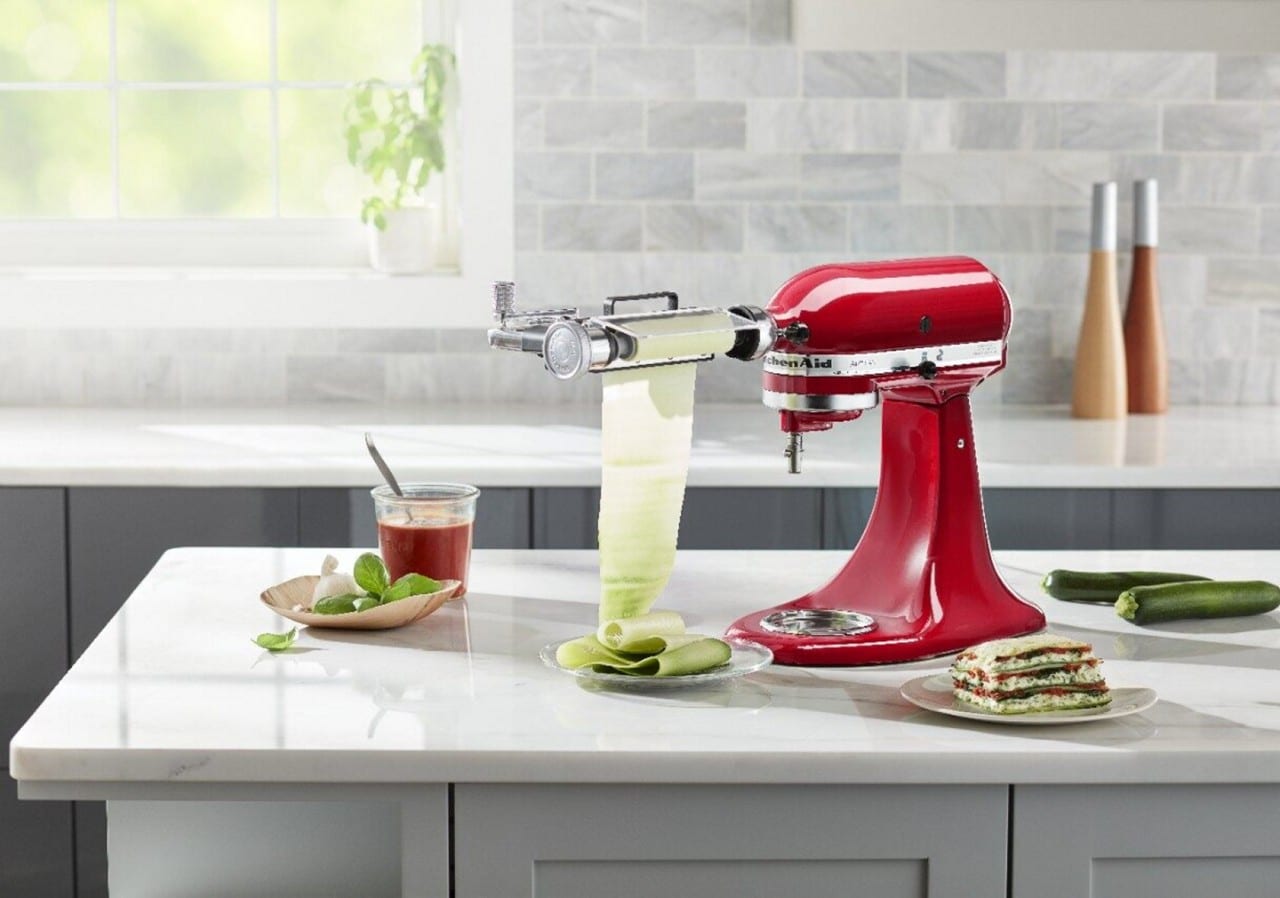 Red KitchenAid® stand mixer with vegetable sheet cutter attachment creating a sheet of zucchini