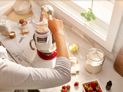 Person putting ingredients into sifter and scale attachment on red KitchenAid® stand mixer