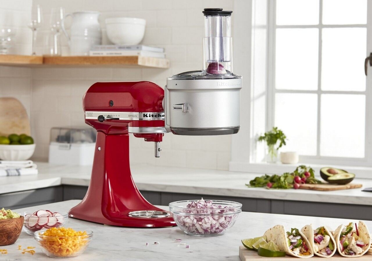 A bowl of onions beneath a red KitchenAid® stand mixer with food processor attachment 