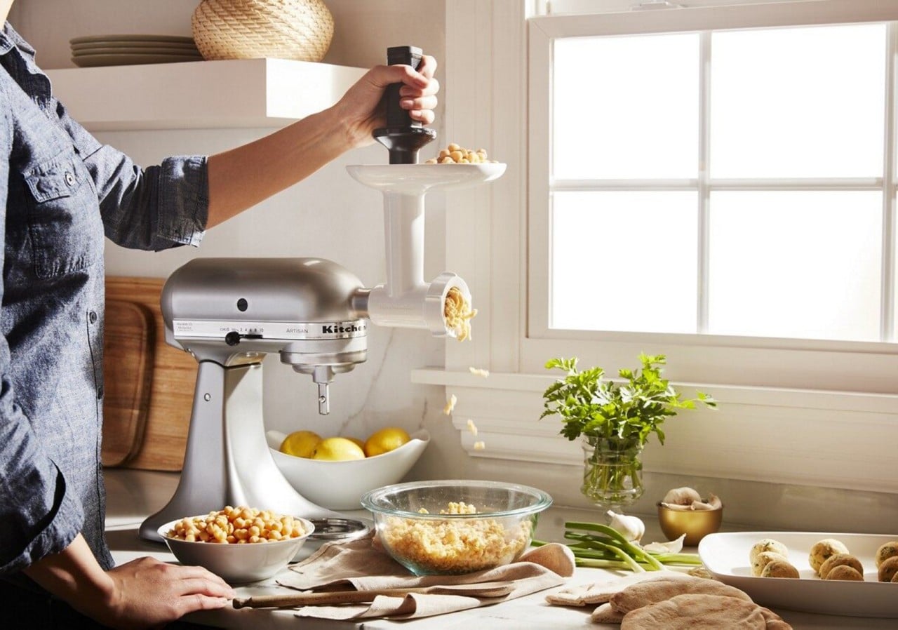 Person putting ingredients in meat grinder attachment on silver KitchenAid® stand mixer