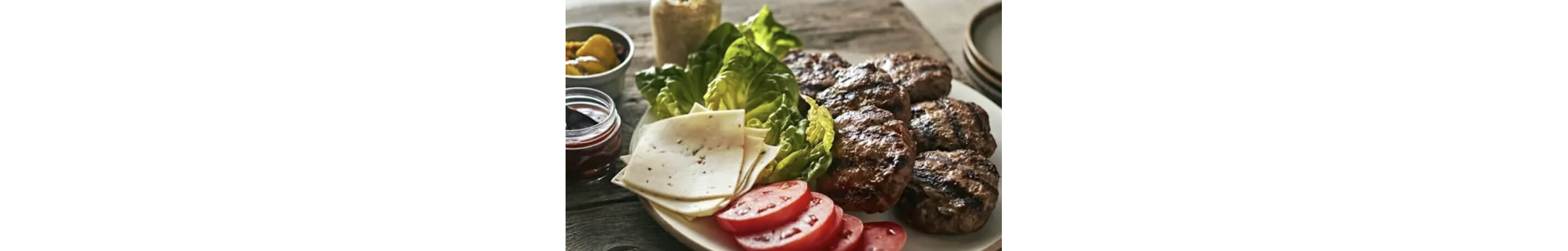 A plate with cooked burger patties, sliced tomatoes, cheese and lettuce.