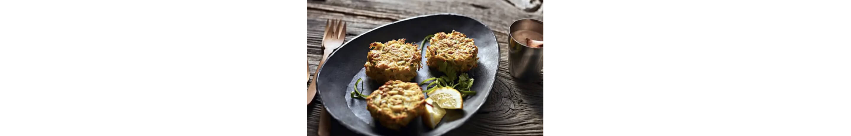 Three crab cakes and garnishes on a dark plate.