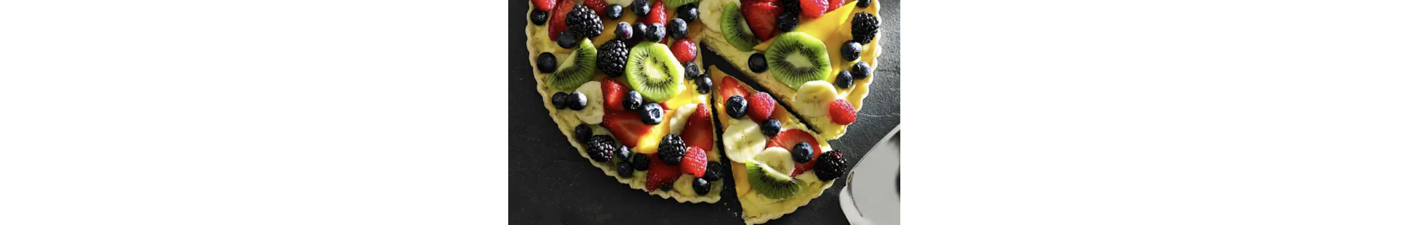 Fresh fruit tart on a countertop with one slice cut.