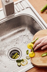 A person pushing scraps into their in-sink disposal.