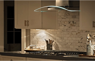 A glass canopy hood with LED lights illuminating a gas cooktop underneath