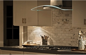 A glass canopy hood with LED lights illuminating a gas cooktop underneath