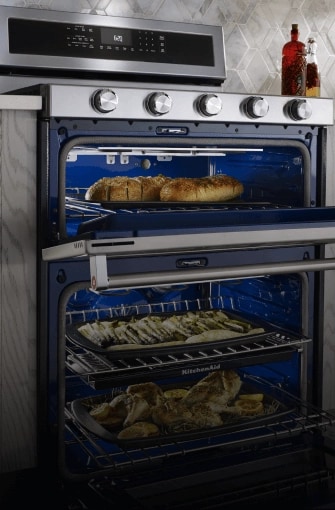 A large KitchenAid® double oven range cooking garlic bread, asparagus and whole chickens inside the oven