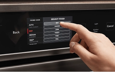A person pressing a button on the touchscreen of a wall oven.