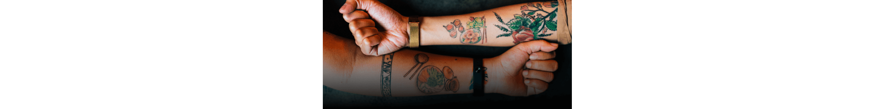 Two arms side by side, showing their gardening and food tattoos.