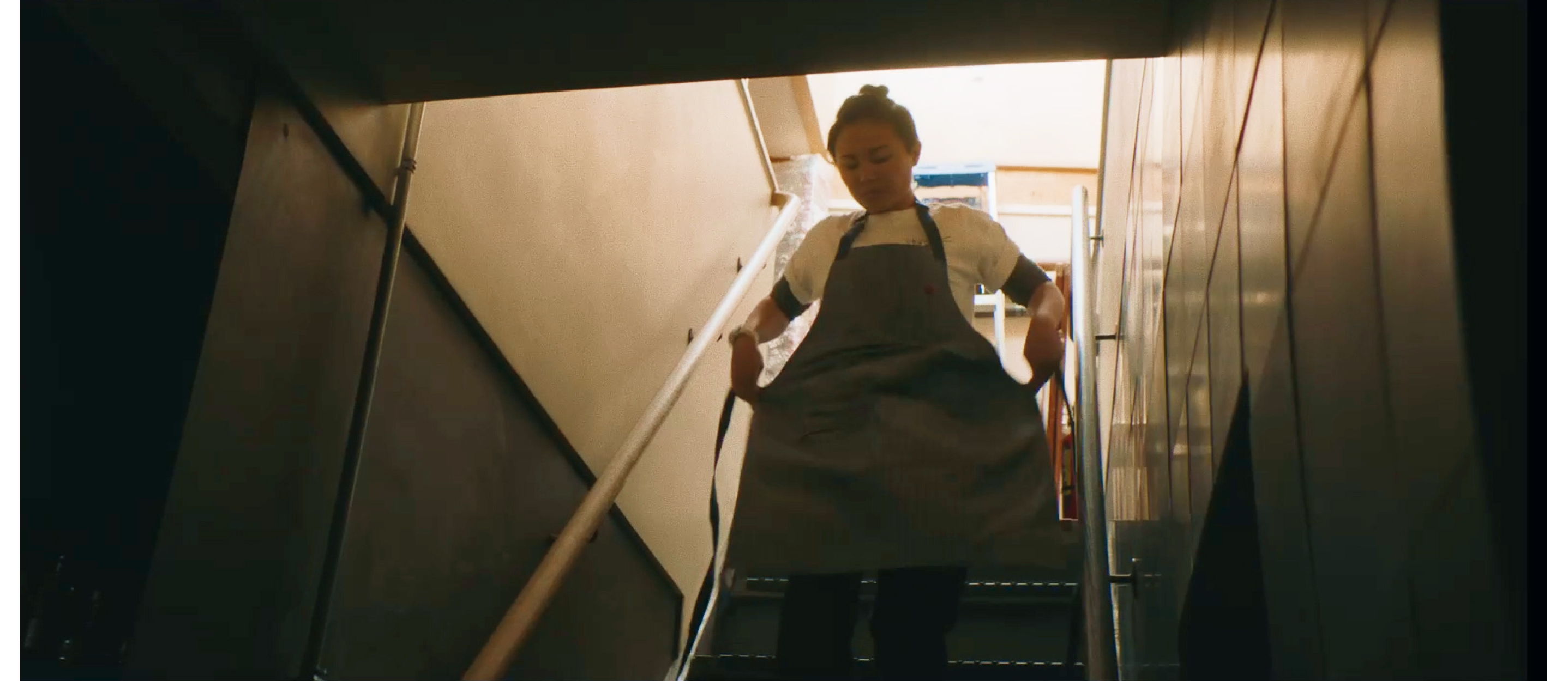 A woman hurrying down the stairs while tying up her apron.