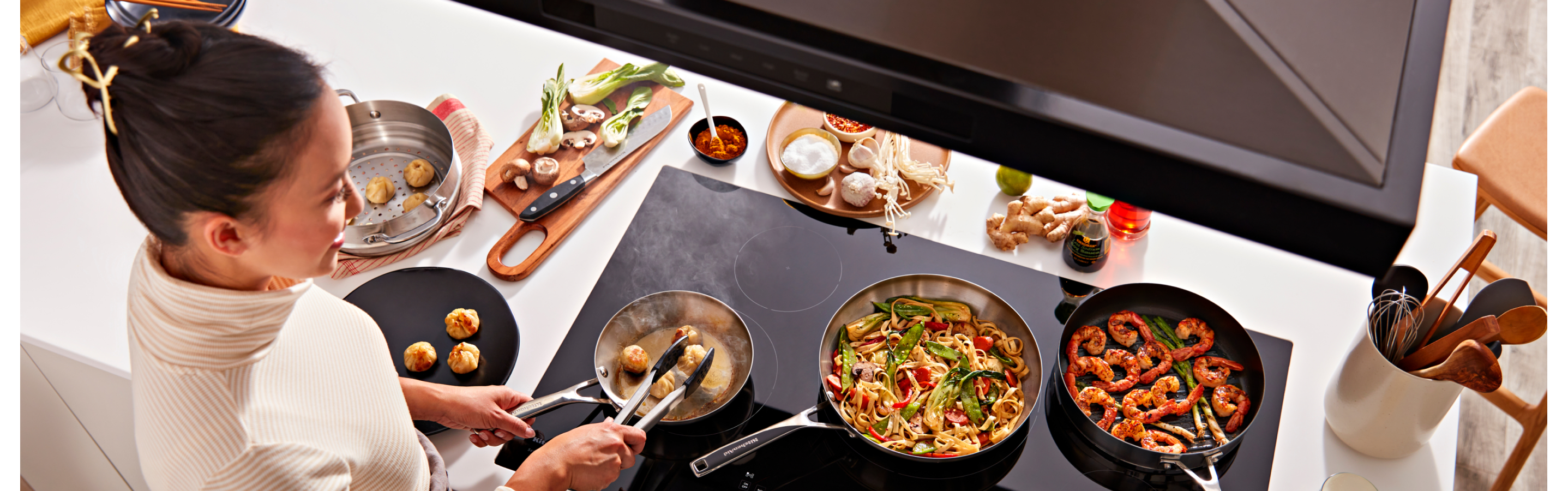 A person cooking on a KitchenAid® cooktop.