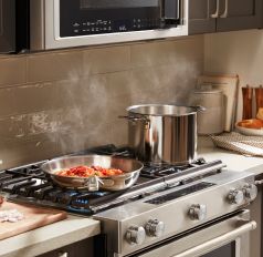 A KitchenAid® range with simmering vegetables in a pan and water boiling in a stockpot.  