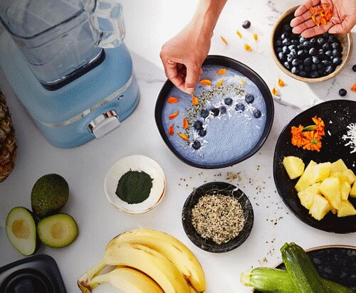 Overhead shot of a delicious-looking bowl of blue blueberry yogurt being topped with accompaniments.