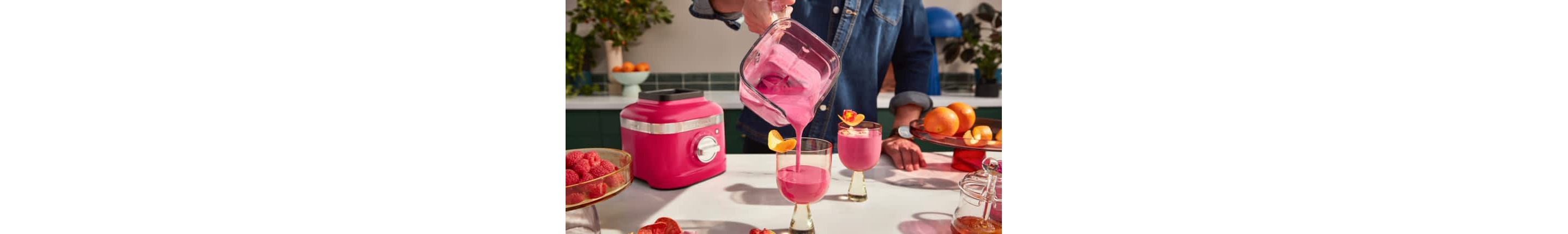 A person pouring a blended hibiscus drink from the K400 Hibiscus Blender into stylish cups with orange peel garnishes.