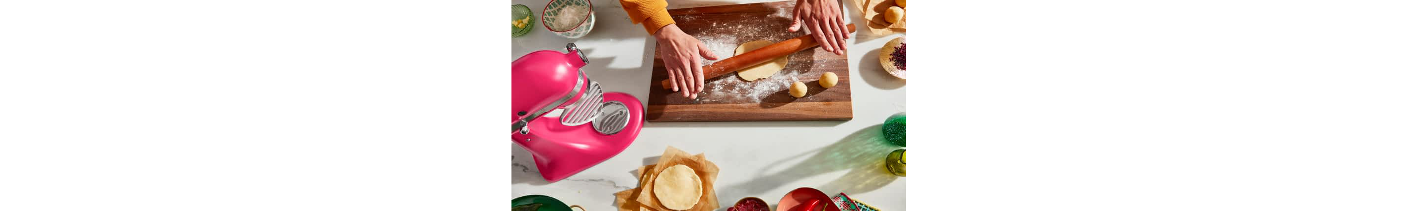 A person rolling dough on a cutting board with a Hibiscus Artisan® Series Stand Mixer on the counter.
