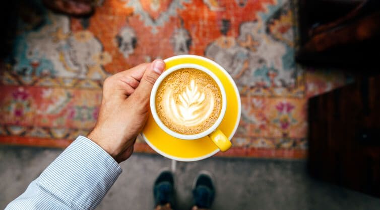 A latte in a yellow teacup and saucer.