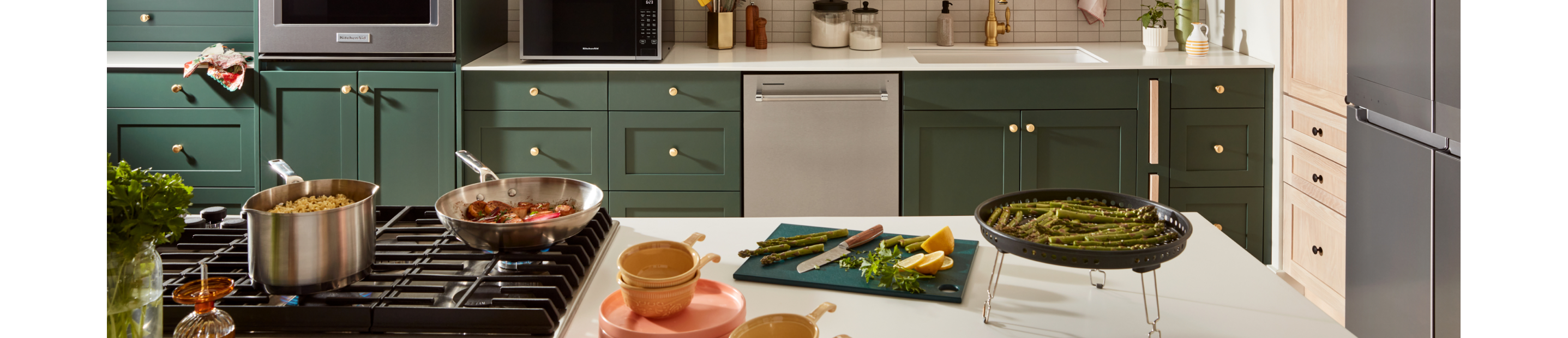 Various food items being cooked on a KitchenAid® rangetop and on the counter of an island. 