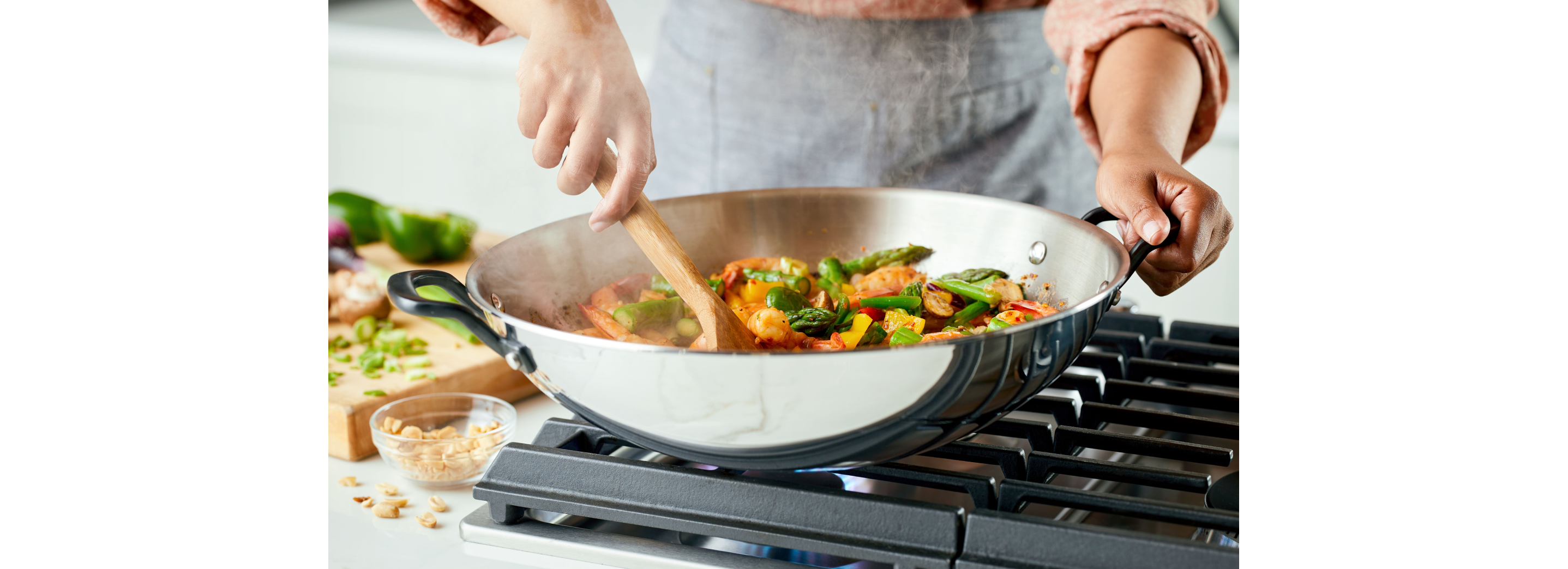 A person cooking with a stainless steel 5-ply base pan.