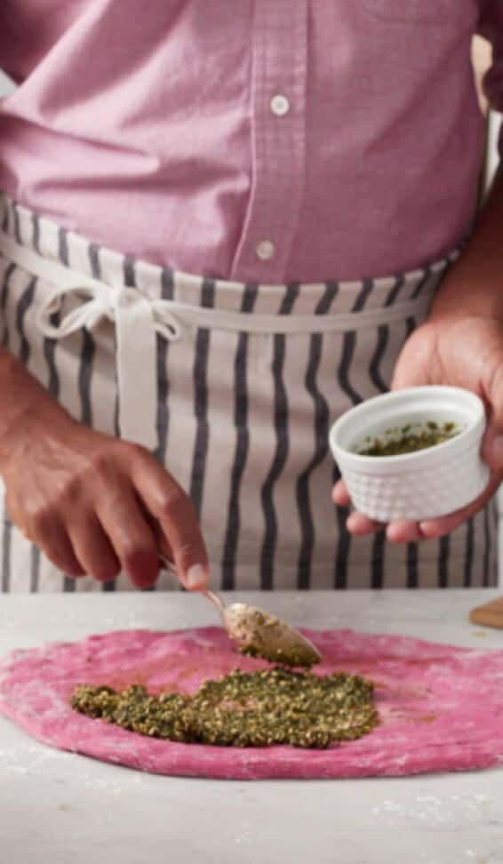 A person making Beetroot pasta with pesto sauce.