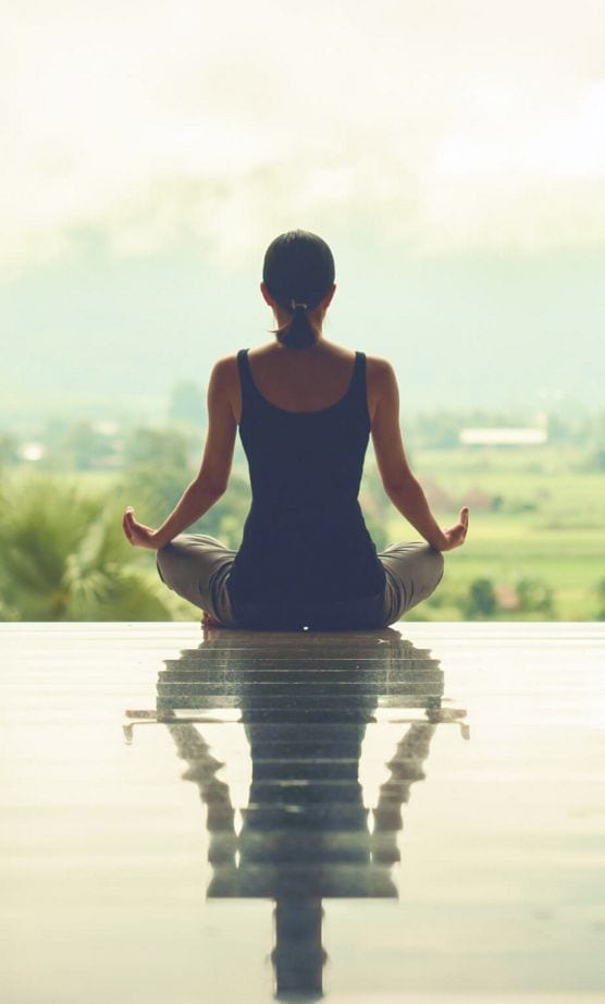 A silhouette of woman basking in the afternoon sun in a quarter lotus meditation pose.