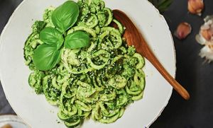 Zucchini noodles covered with parmesan and garnished with basil in a white bowl with a wooden spoon.