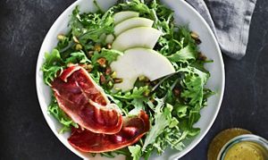 An arugula salad in a white bowl sprinkled with pistachios and thinly sliced green apples.