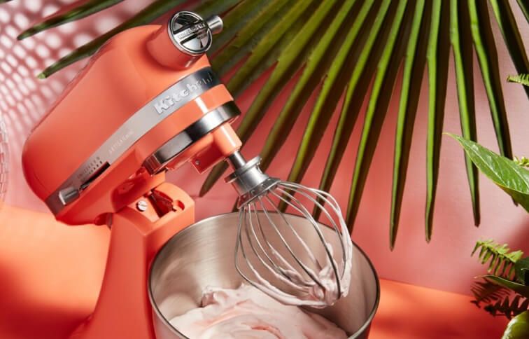 A Bird of Paradise Stand Mixer tilted upwards with a whisk attachment doused in pink frosting.