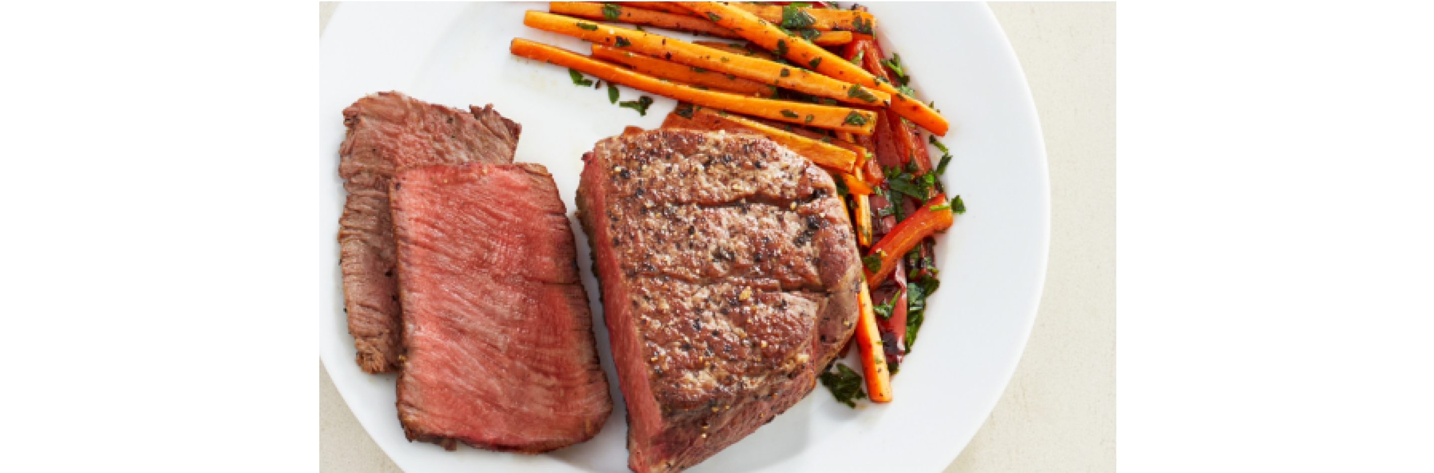 A medium rare steak on a plate with prepared carrots garnished with parsley. 