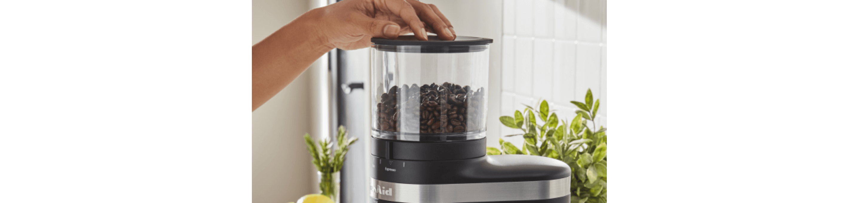 A woman preparing to process coffee beans in a black coffee grinder. 