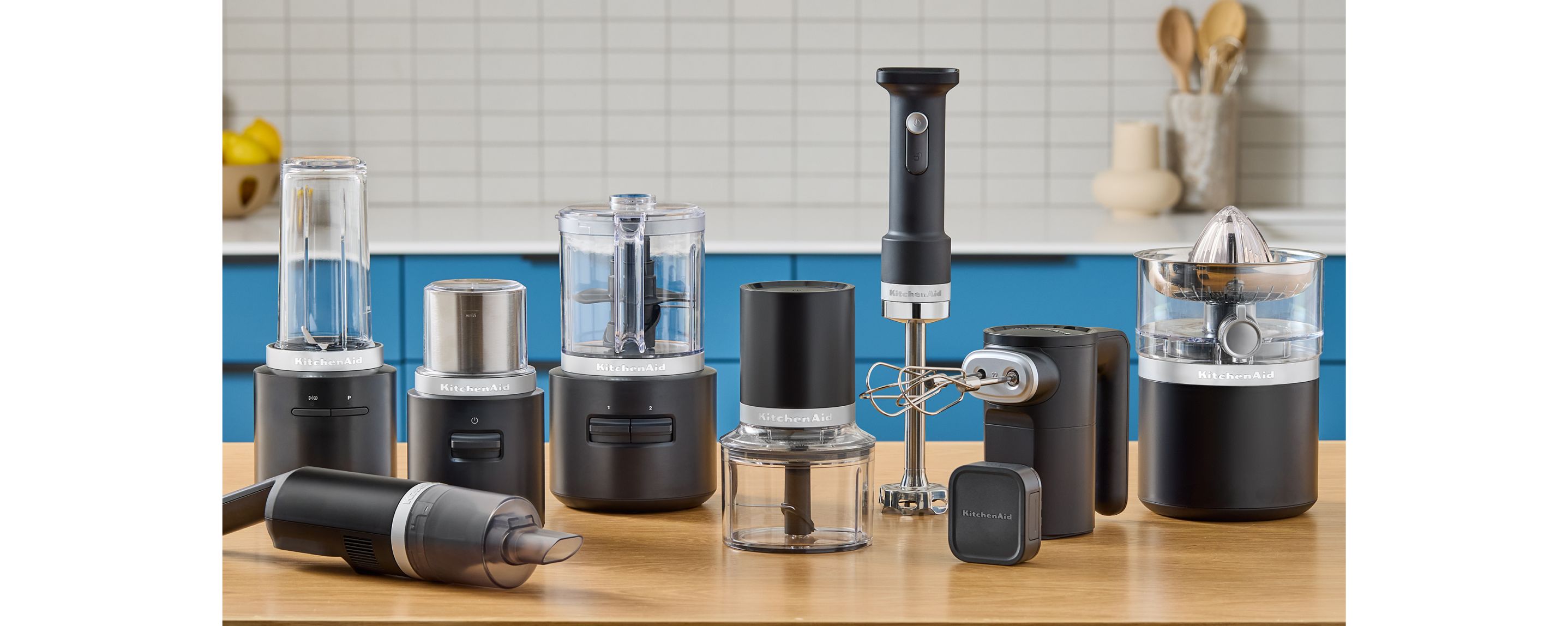 The entire matte black KitchenAid Go™ Cordless lineup of appliances on a kitchen counter, with blue cabinets in the background.