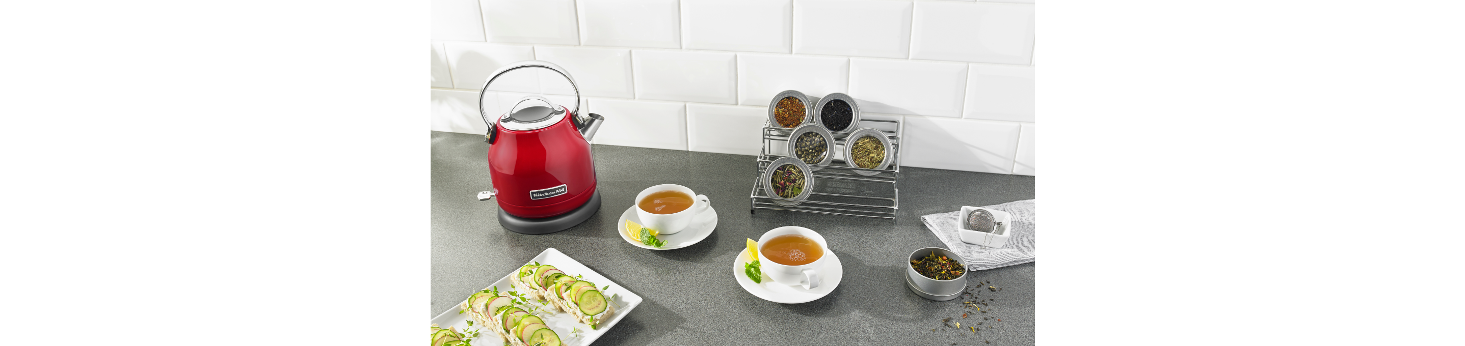 A KitchenAid® Kettle next to cups of tea and snacks.