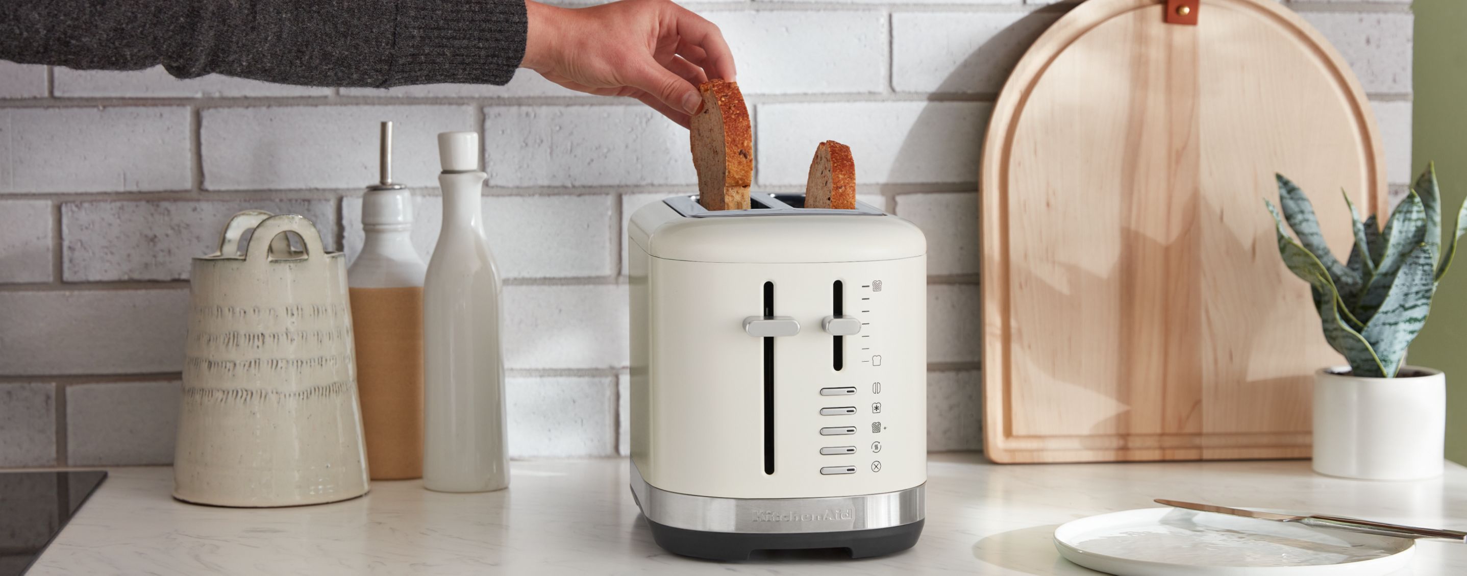 A person pulling a slice of toaster out of a KitchenAid® toaster.