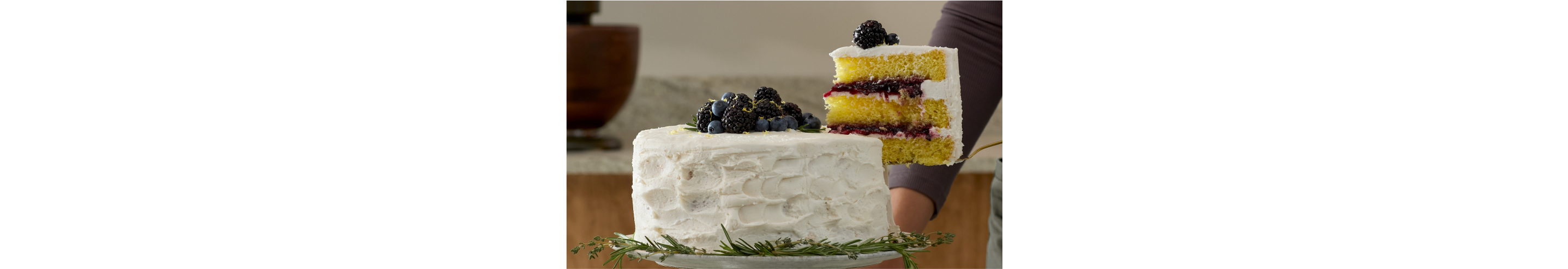 A slice being lifted from a lemon rosemary cake topped with dark berries.