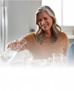 A woman pours water from a clear pitcher into a glass