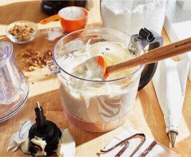 A food chopper work bowl holding freshly made cream and a wooden spatula.