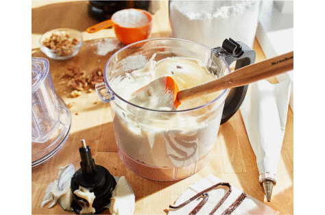 A food chopper work bowl holding freshly made cream and a wooden spatula.