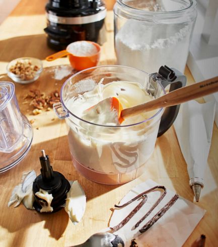 A food chopper work bowl holding freshly made cream and a wooden spatula.