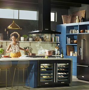 A woman selecting spices for sauce resting in a pot on the stove in a large, navy blue kitchen.