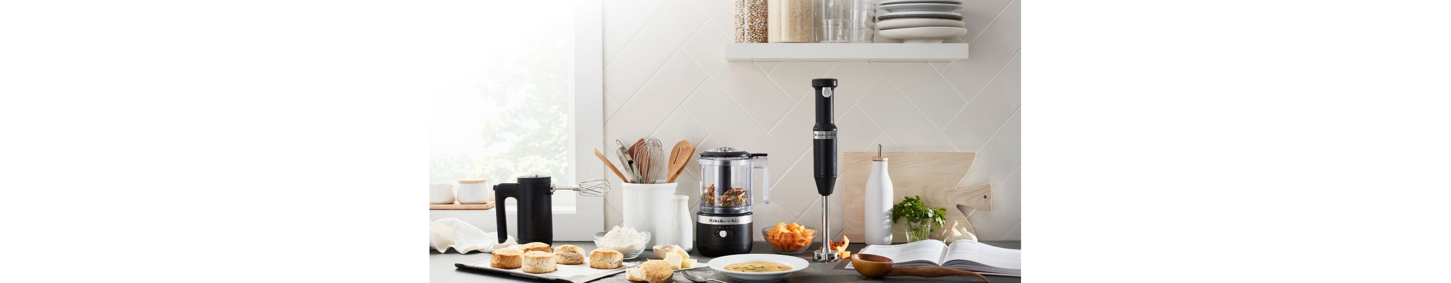 A sun-filled countertop featuring the Matte Black Cordless Chopper, Hand Mixer and Hand Blender.