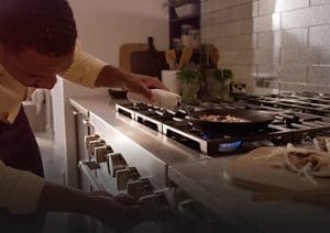Man adjusting temperature while sautéing on a stainless steel range.