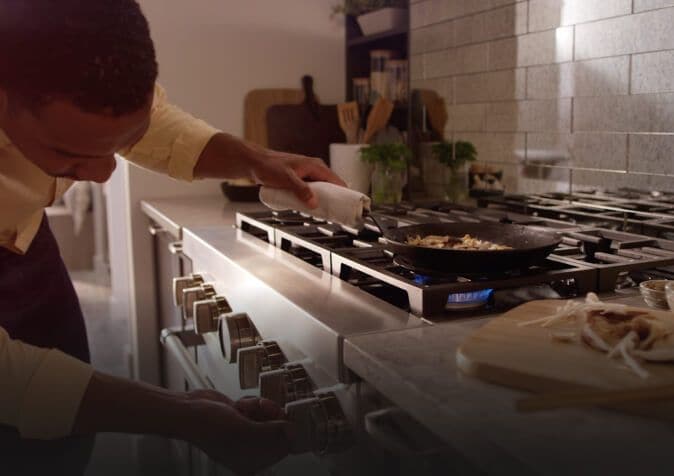 Man adjusting temperature while sautéing on a stainless steel range.