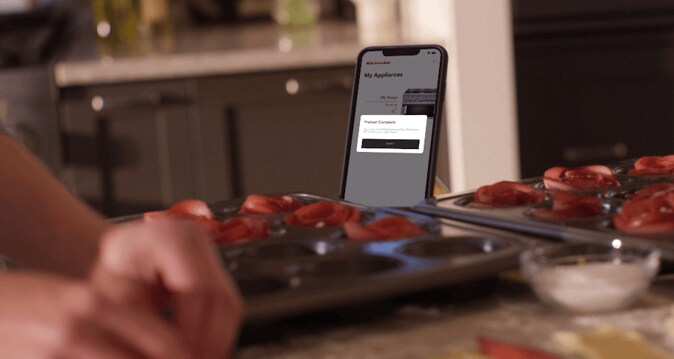 Person using Kitchenaid app while preparing pastries on counter.