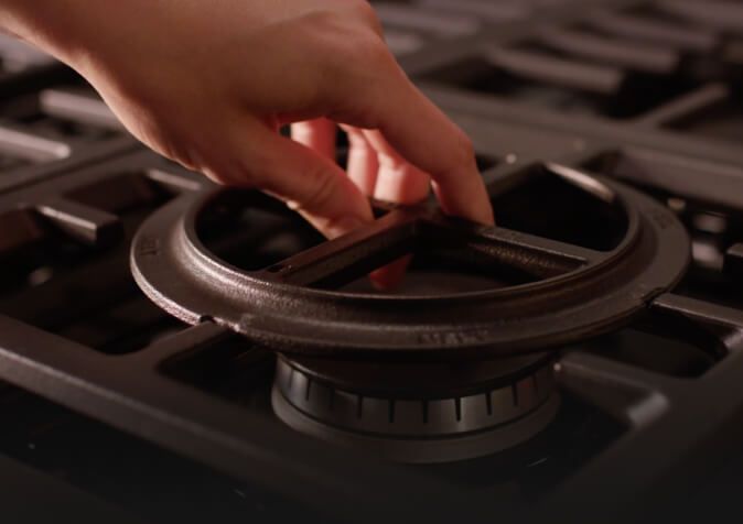 Close-up of hand placing convertible grate above burner.