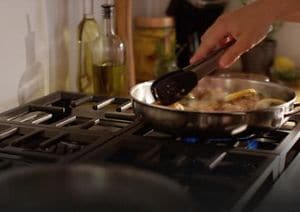 Person sautéing vegetables on rangetop burner.