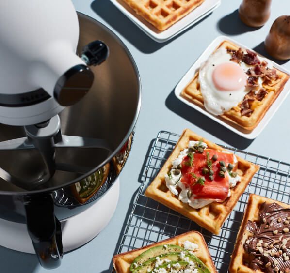 A Limited Edition Stand Mixer with Black Stainless Bowl on a kitchen counter next to waffles.