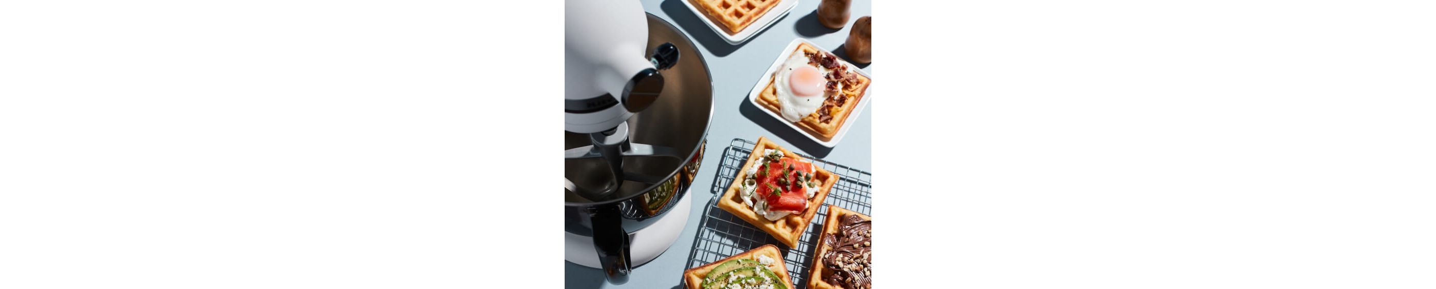 A Limited Edition Stand Mixer with Black Stainless Bowl on a kitchen counter next to waffles.