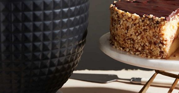 A studded black ceramic bowl next to chocolate cake on a platter.